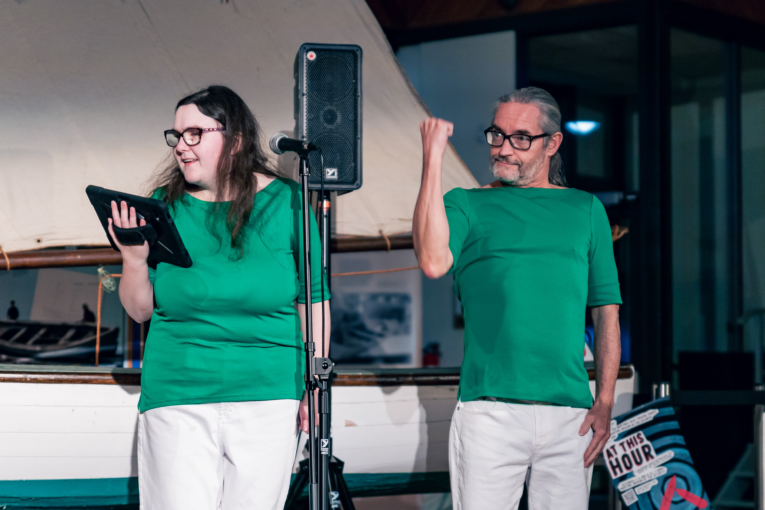 Phillipa Colman looks to her right and smiles, she is holding an iPad. Alan Williams is to Phillipa's left, he gestures  with his fist in the air, at about the same level as his eyes.