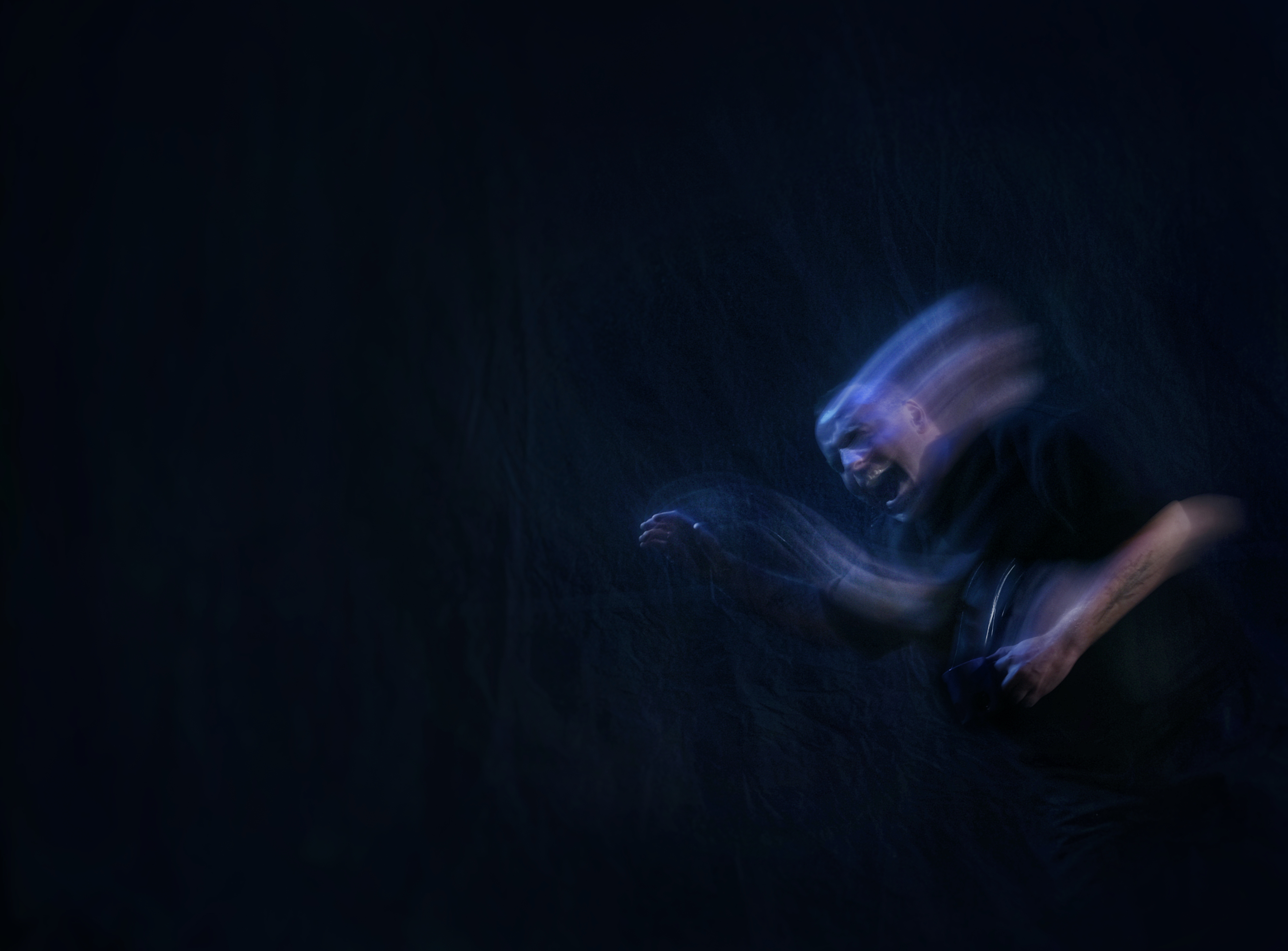 A black background. A ghostly, blurred image of a man in blue/purple light, seemingly screaming in agony. 