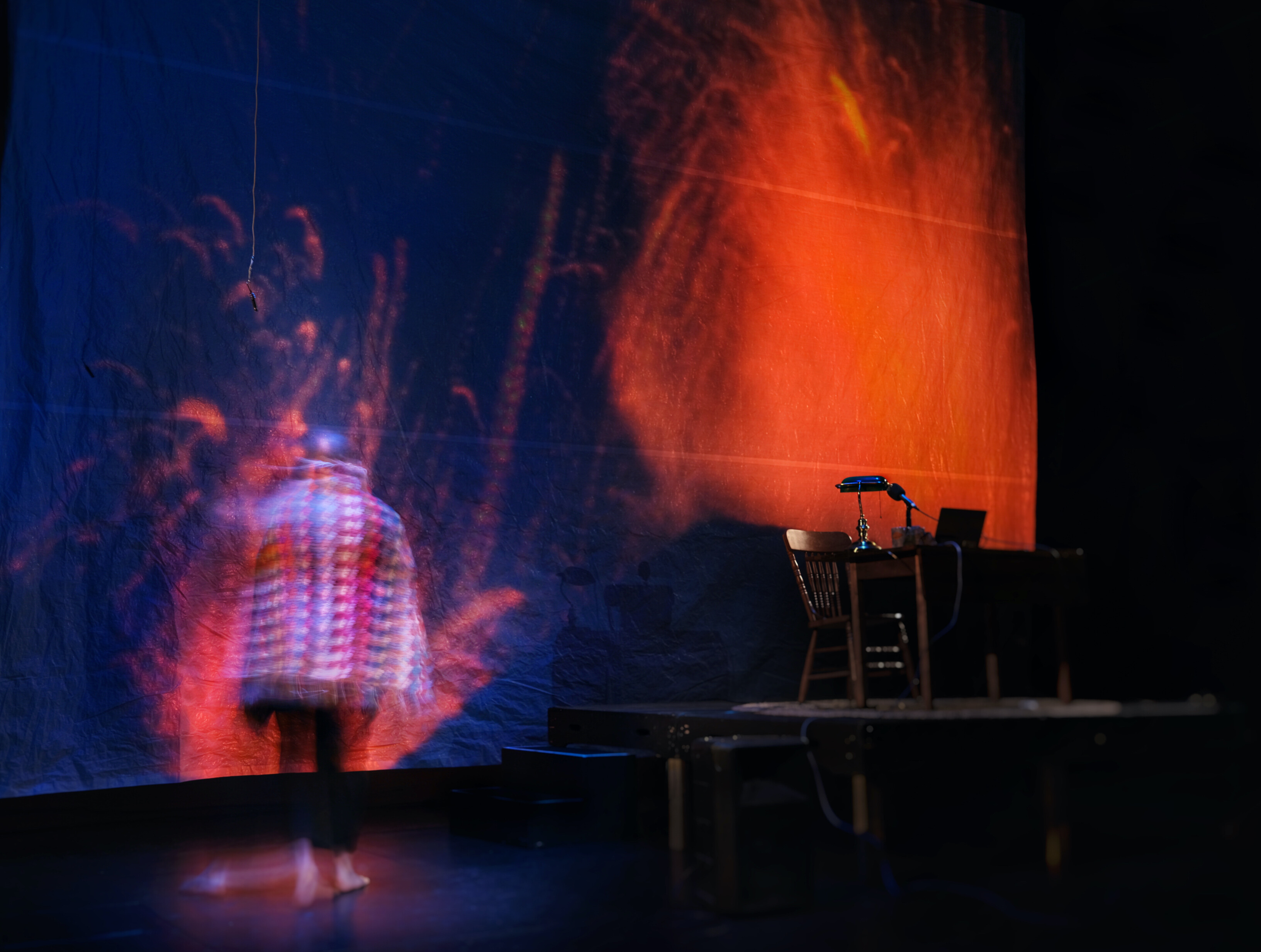 a man, wrapped in a colourful knit blanket, stands with his back to the camera. He is staring at a giant projection screen where fire and lava fill his view. Because of the angle of the shot, it sometimes appears as though he himself is inside the fire. 