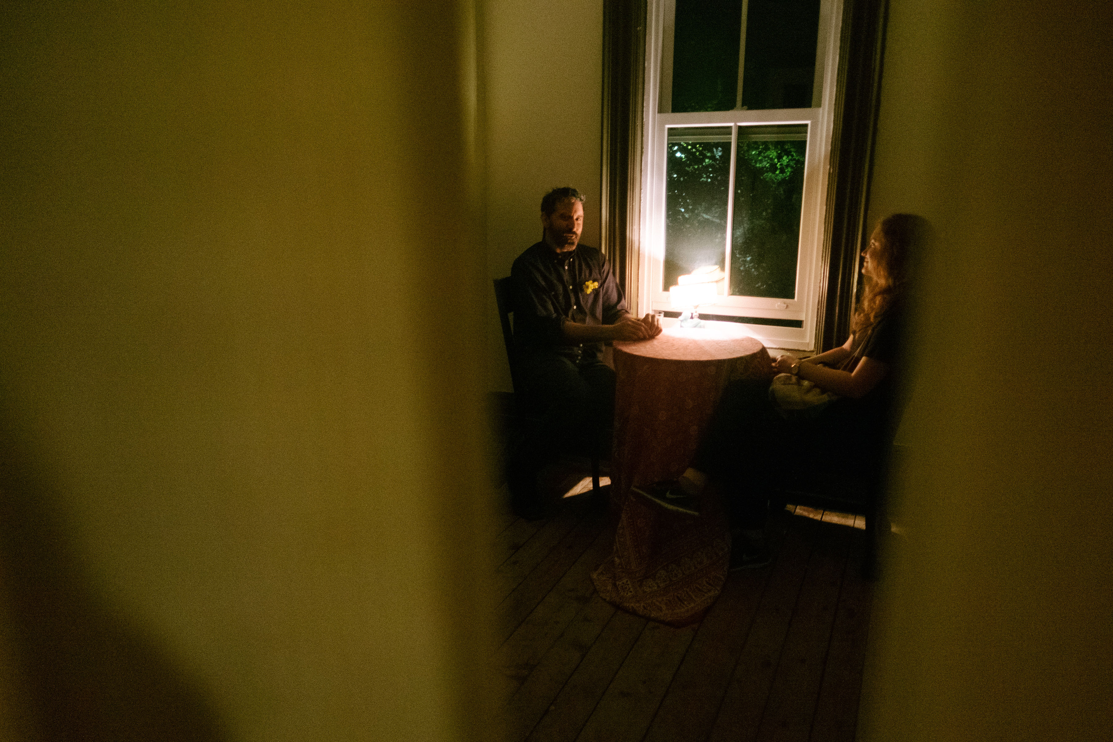 View through an open door. A man and woman talk at a table inside.